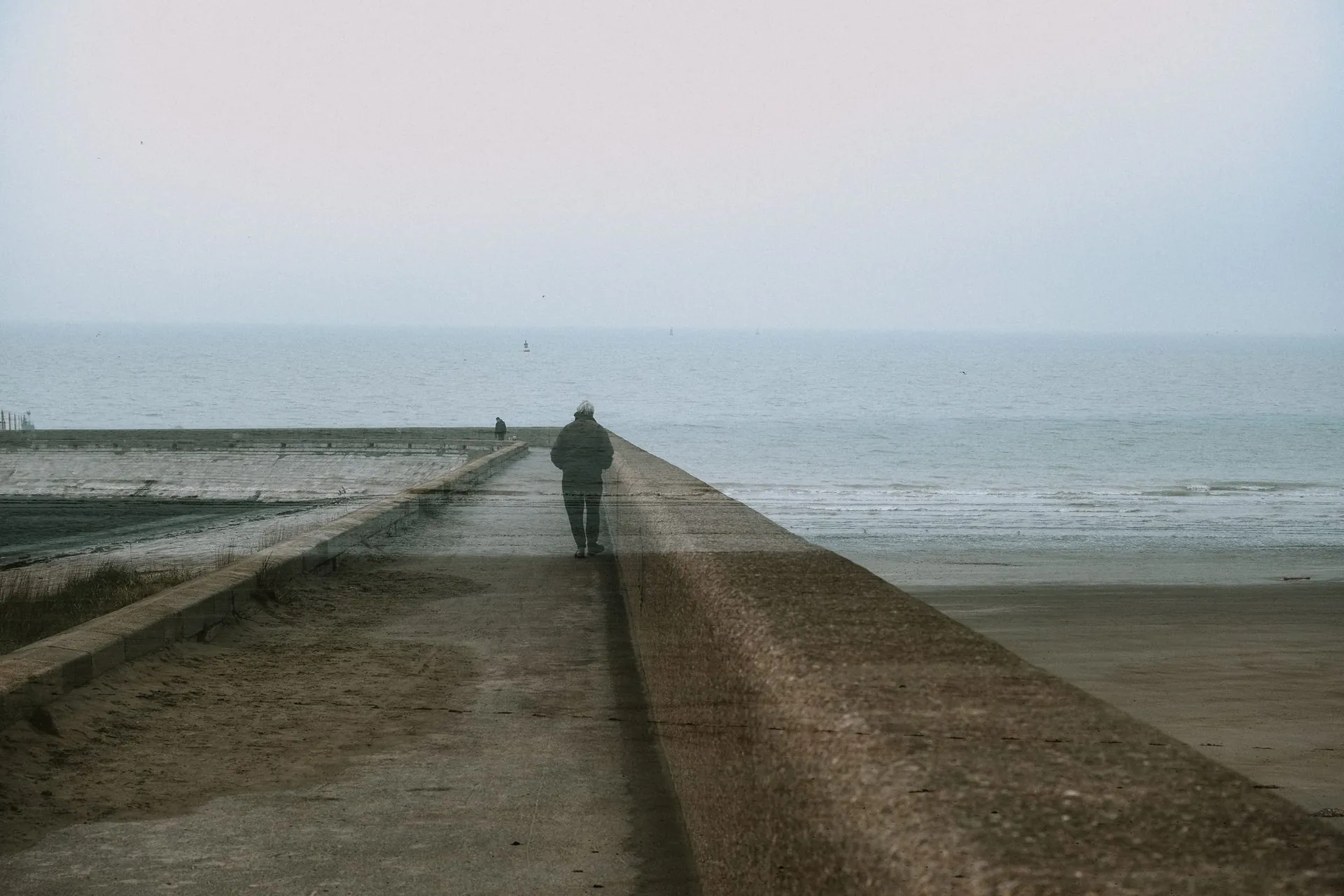 a lone figure walking a seawall into mist